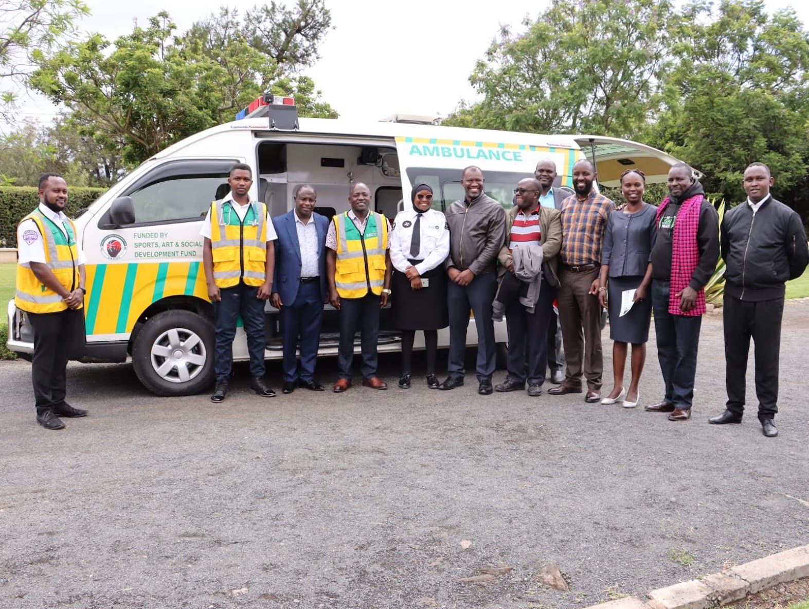 Group photo beside an ambulance funded by the Sports, Arts and Social Development Fund